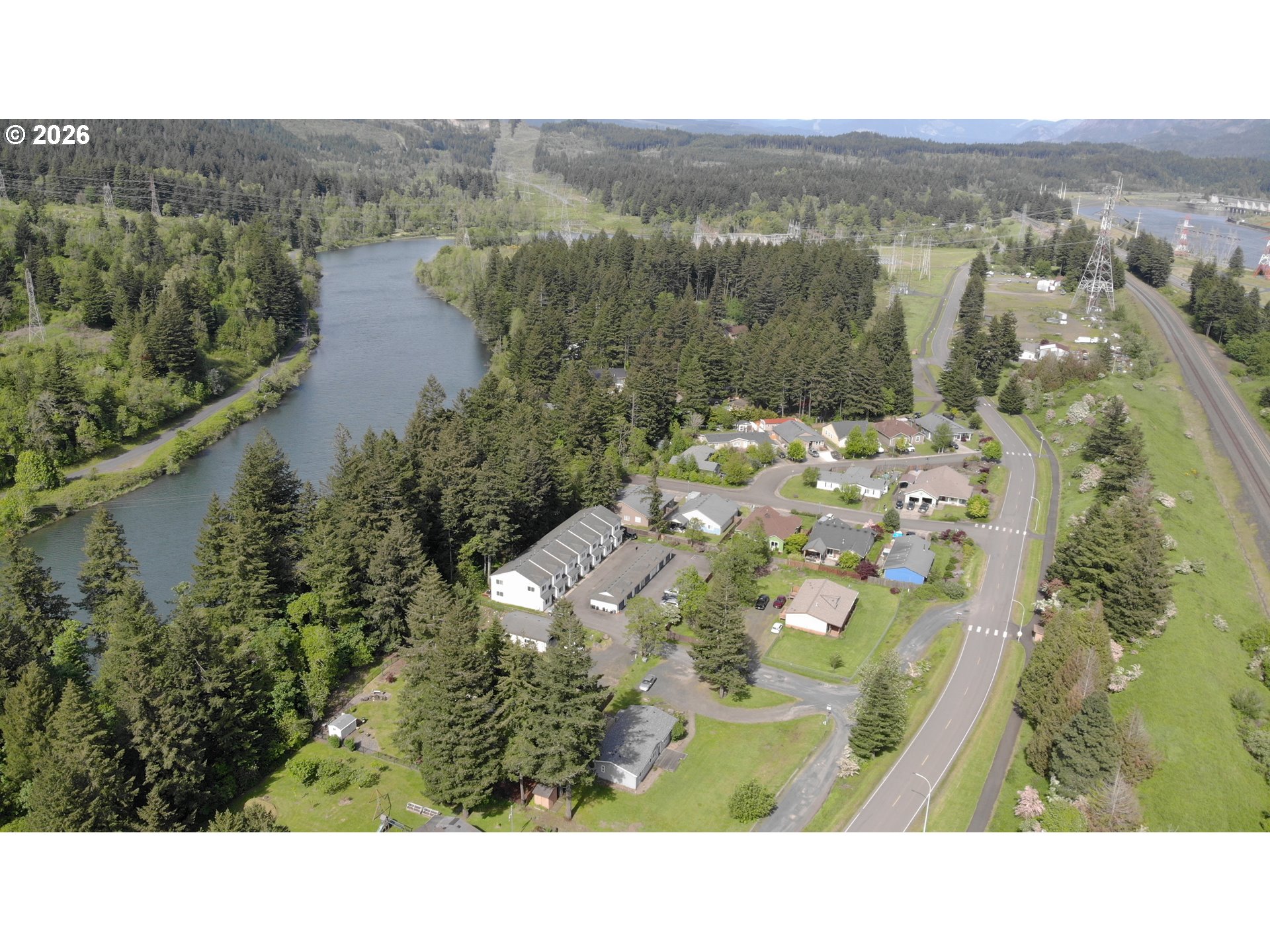 Aerial view of homes beside a winding river and dense evergreen forest.