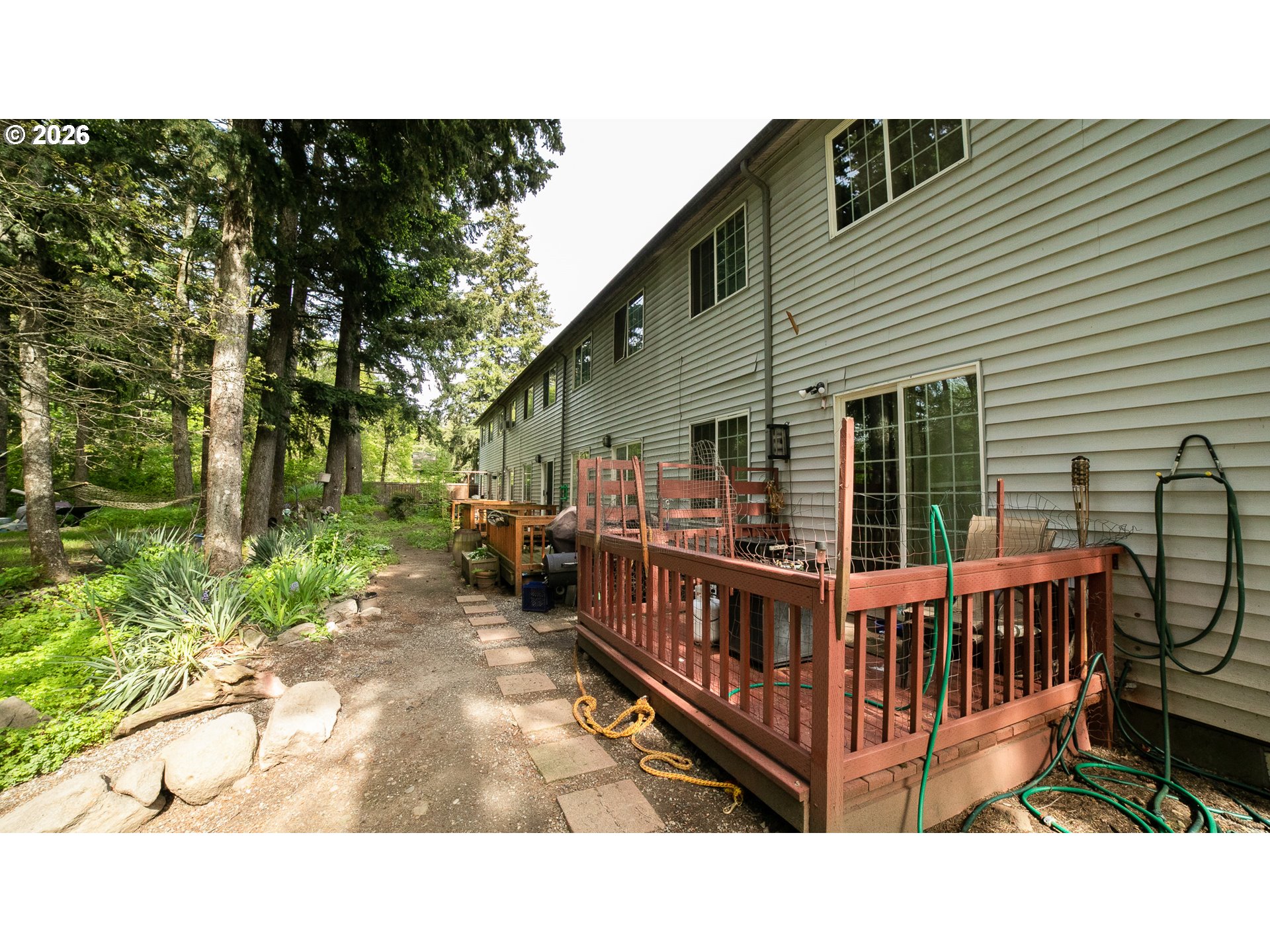 Home exterior with a red deck beside a wooded yard and stone path.
