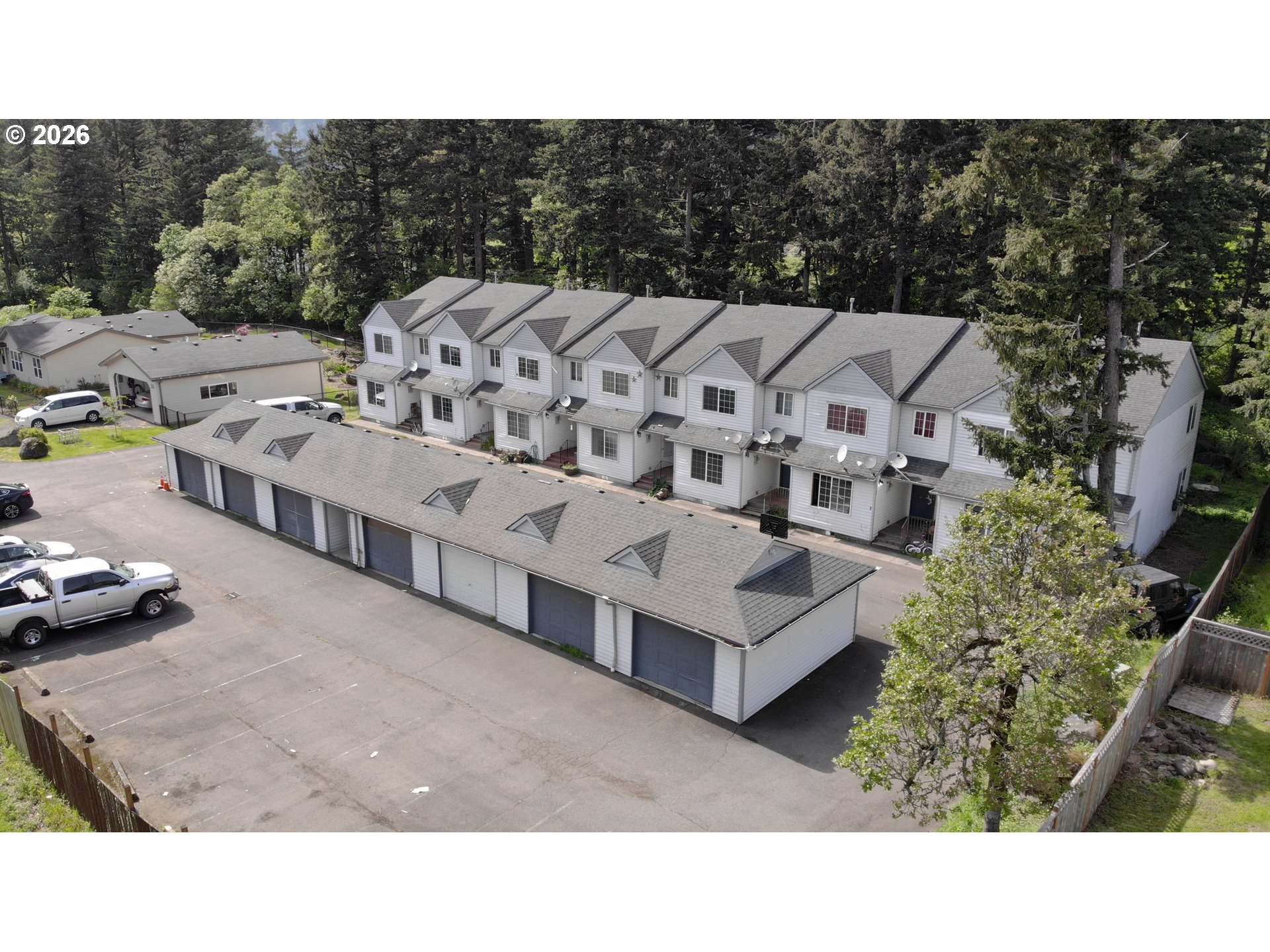 Aerial view of attached white townhomes, a long garage building, and paved parking area.