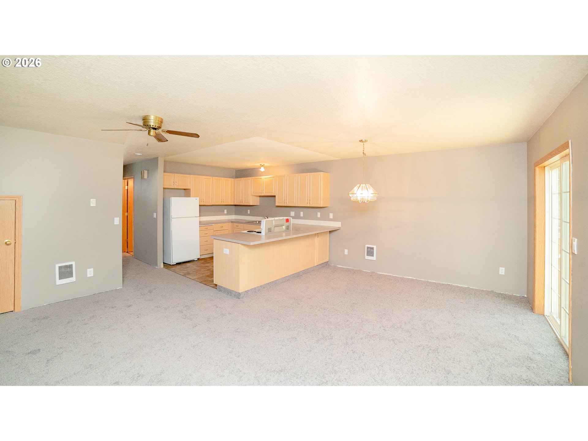 Open-plan living and dining area with a light wood kitchen island and sliding glass door.