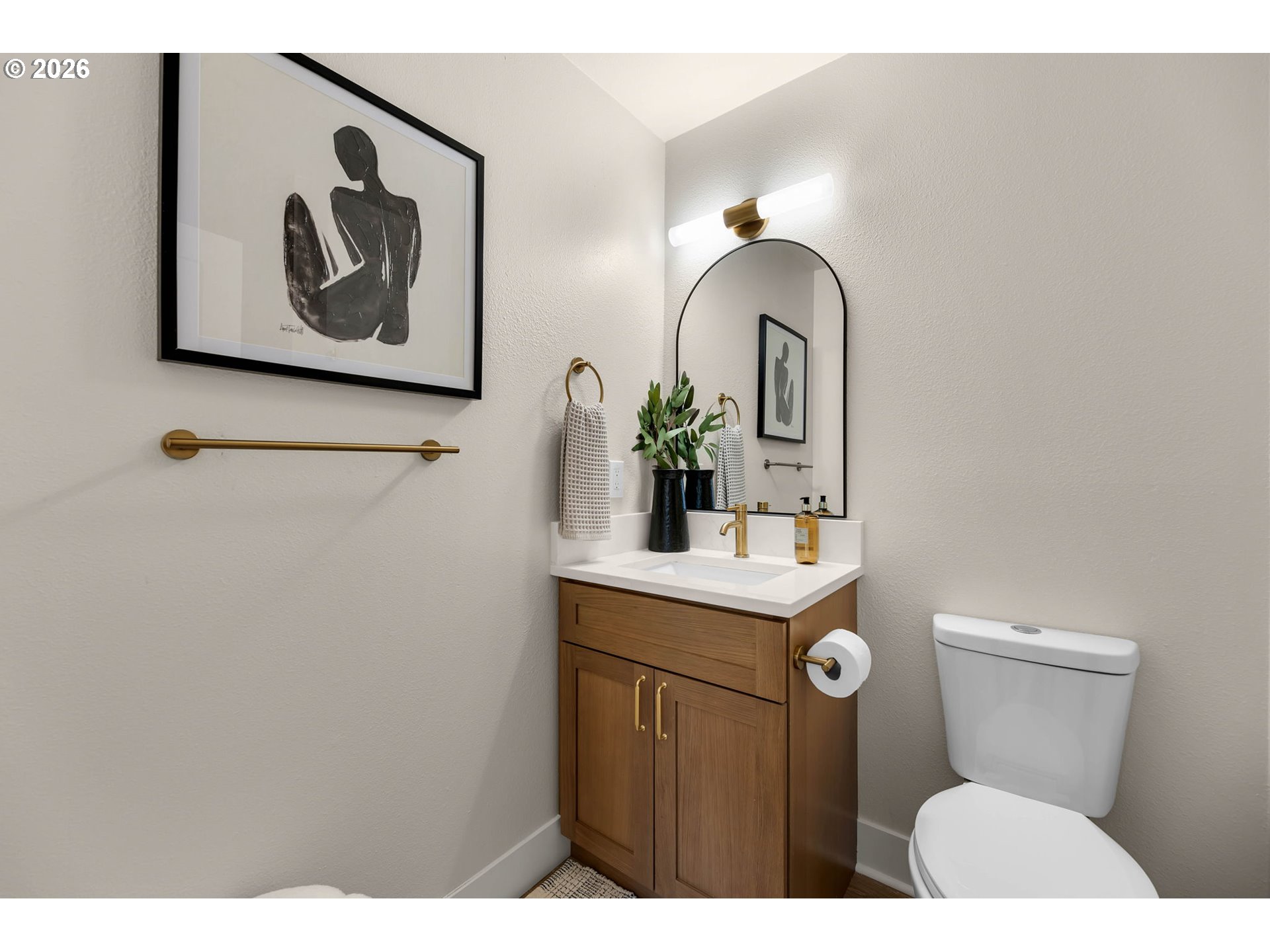 Bathroom with a walnut vanity, brass fixtures, and an arched mirror beside the toilet.