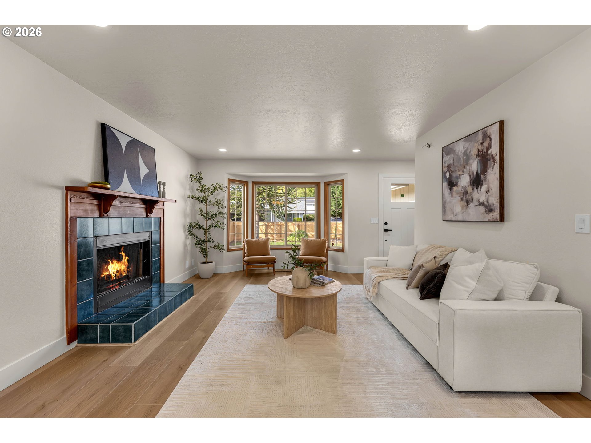 Staged living room with a blue-tiled fireplace, white sofa, and bay window.
