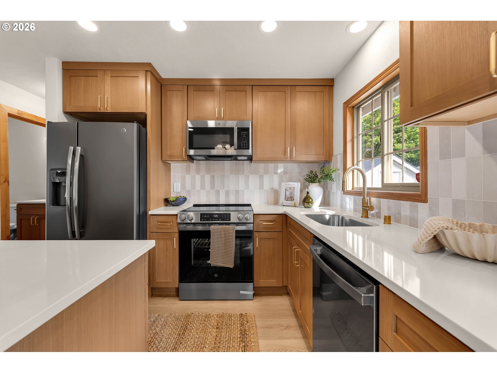 Kitchen with warm wood cabinets, stainless steel appliances, and a large window above the sink.