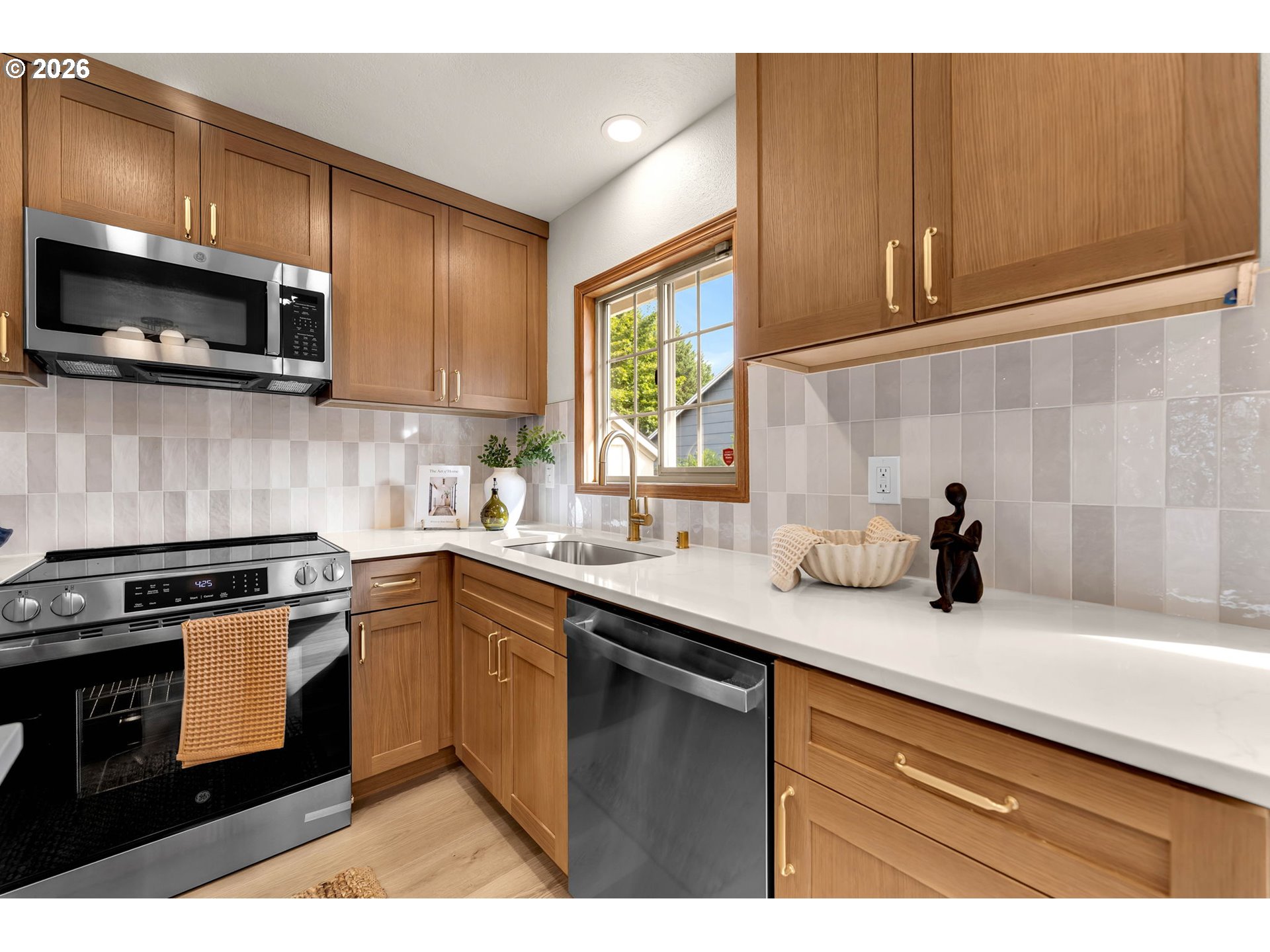Kitchen with warm wood cabinets, white countertops, stainless steel appliances, and a window above the sink.