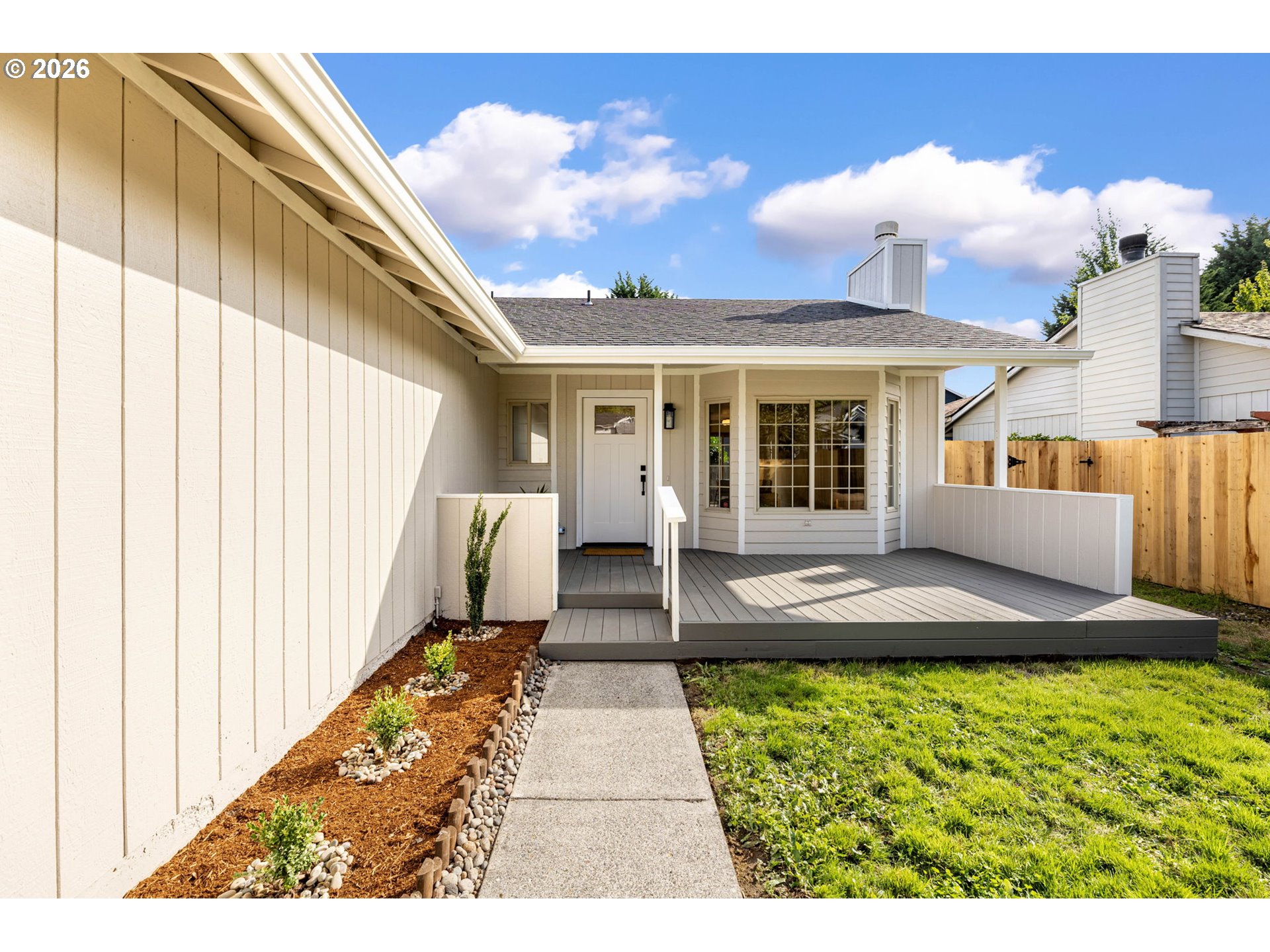 Rear exterior of a light-sided home with a covered deck, entry path, and fenced yard.