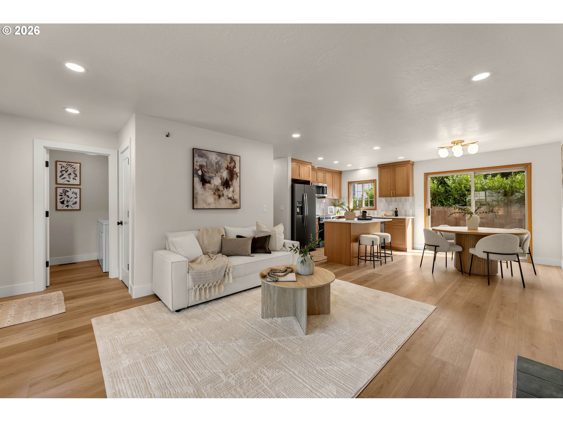 Open-plan living room, kitchen, and dining area with warm wood cabinetry and wide sliding doors.