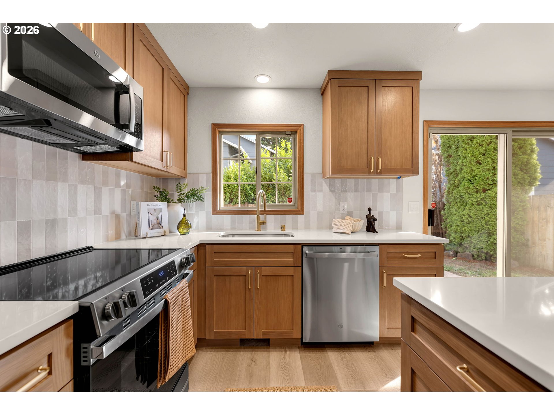 Kitchen with warm wood cabinets, stainless steel appliances, and a sink beneath a window overlooking greenery.