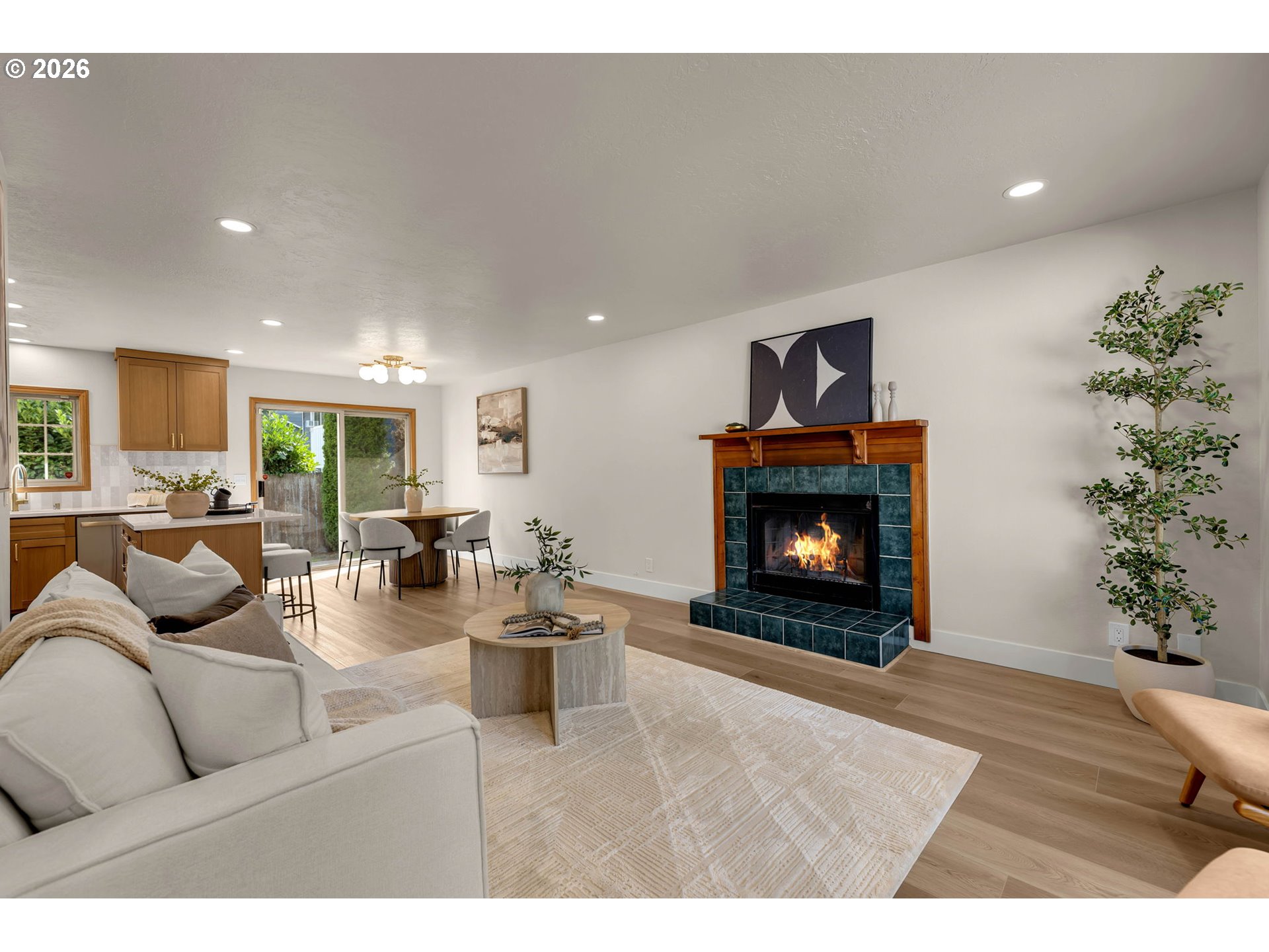 Open-plan living room and kitchen with a white sofa and teal-tiled fireplace.