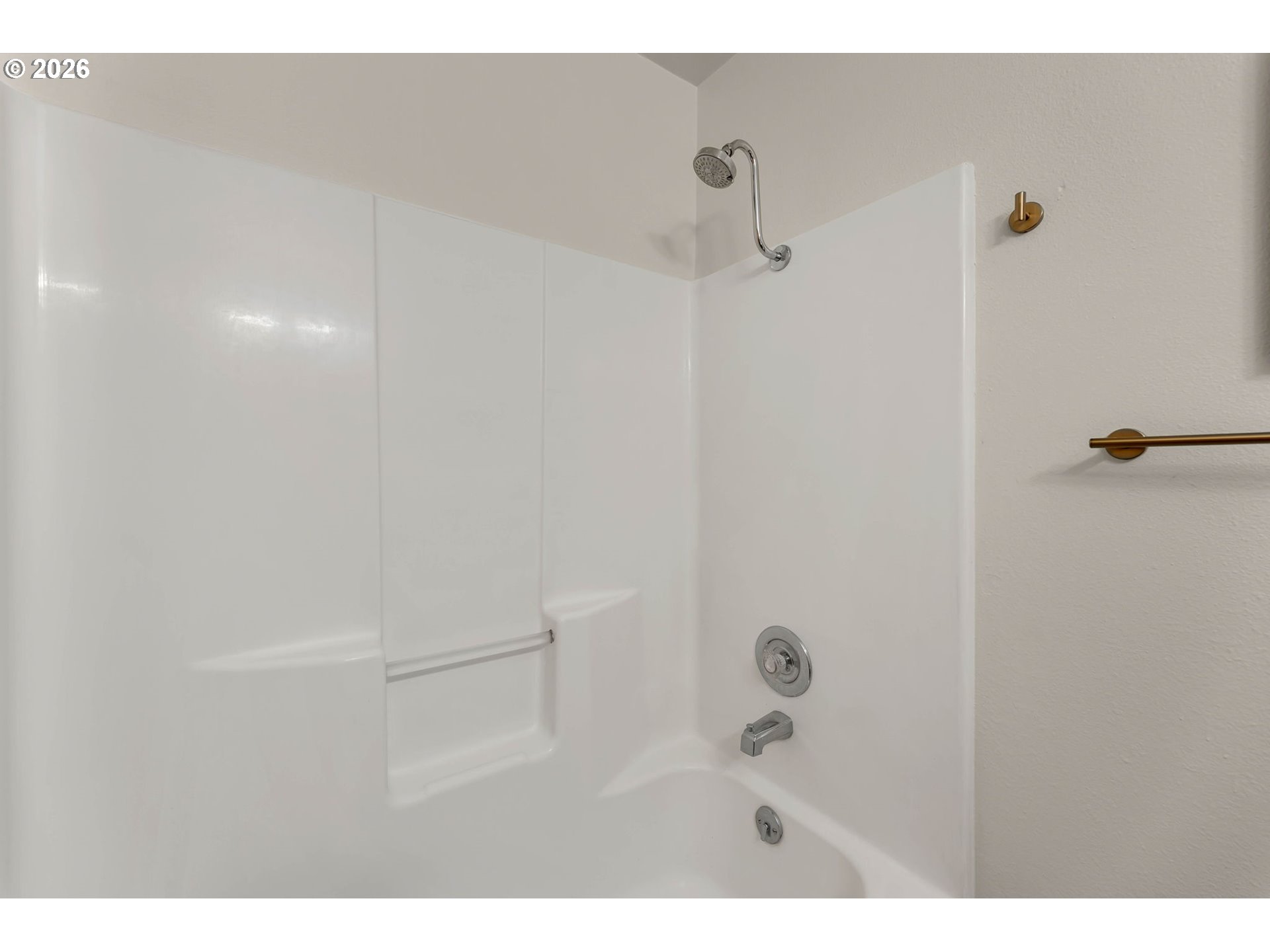 Bathroom tub and white shower surround with built-in shelves and chrome fixtures.