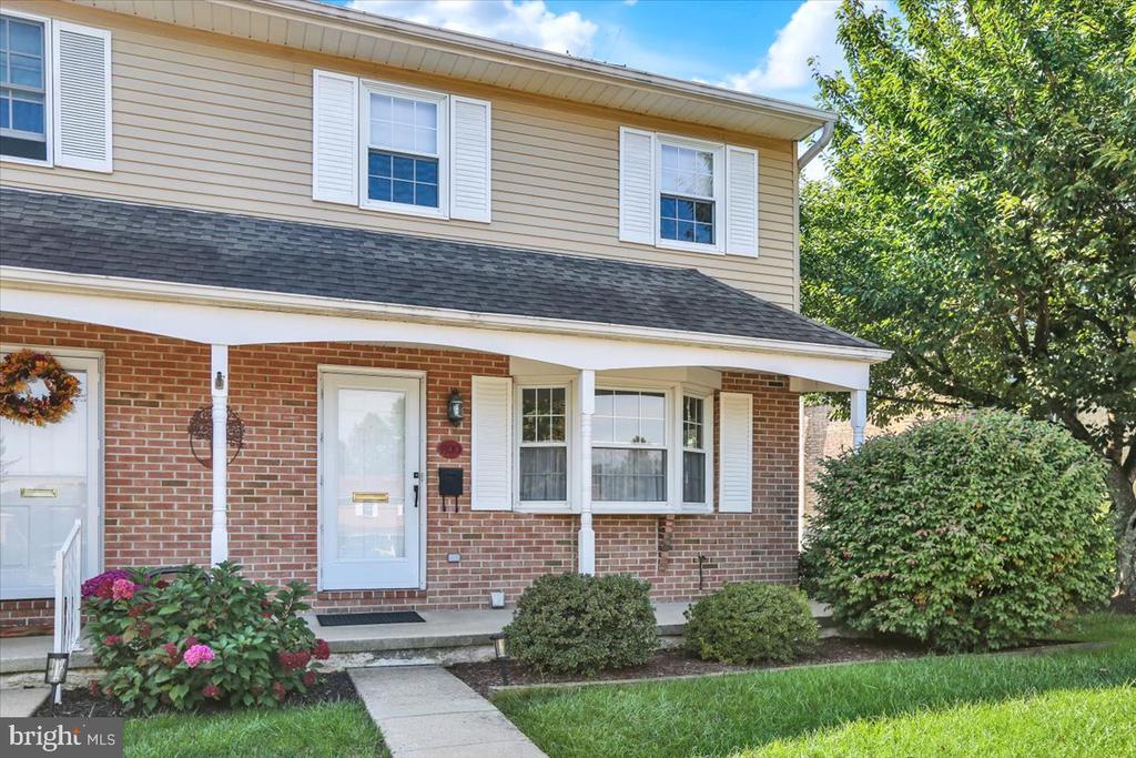 Two-story brick-and-siding house with white shutters, a covered entry, and flowering shrubs.