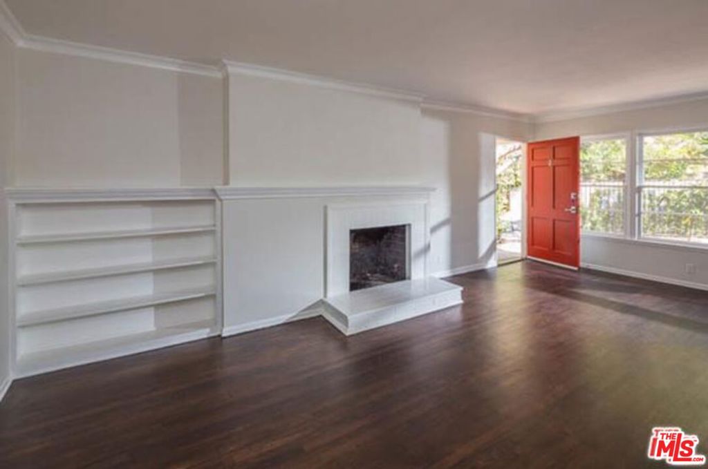 Vacant living room with a white fireplace and built-in shelves, dark floors, and a red door.