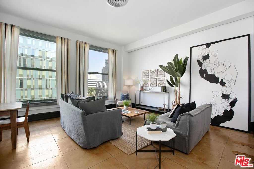Furnished living room with gray sofas, large windows, and views of nearby city buildings.