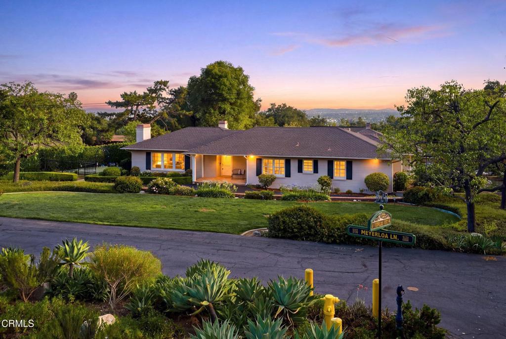 Single-story home with a broad lawn and mature trees, warmly lit at dusk.