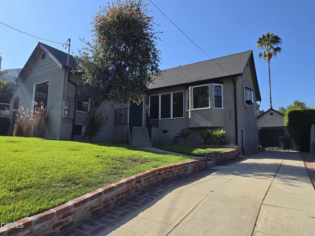 Gray stucco house with a front lawn, brick retaining wall, and long driveway.