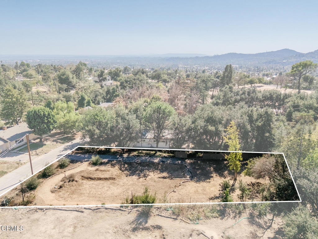 Vacant lot outlined in white, surrounded by trees with distant hills in view.