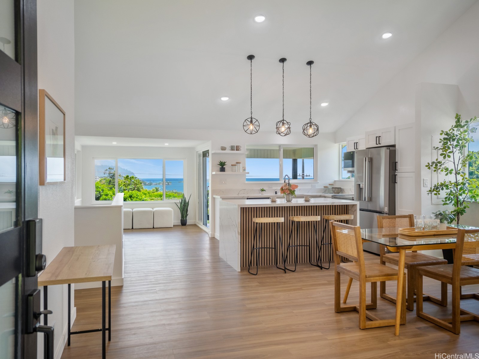 Open-plan kitchen with a wood-slat island and dining table, overlooking the ocean and mountains.