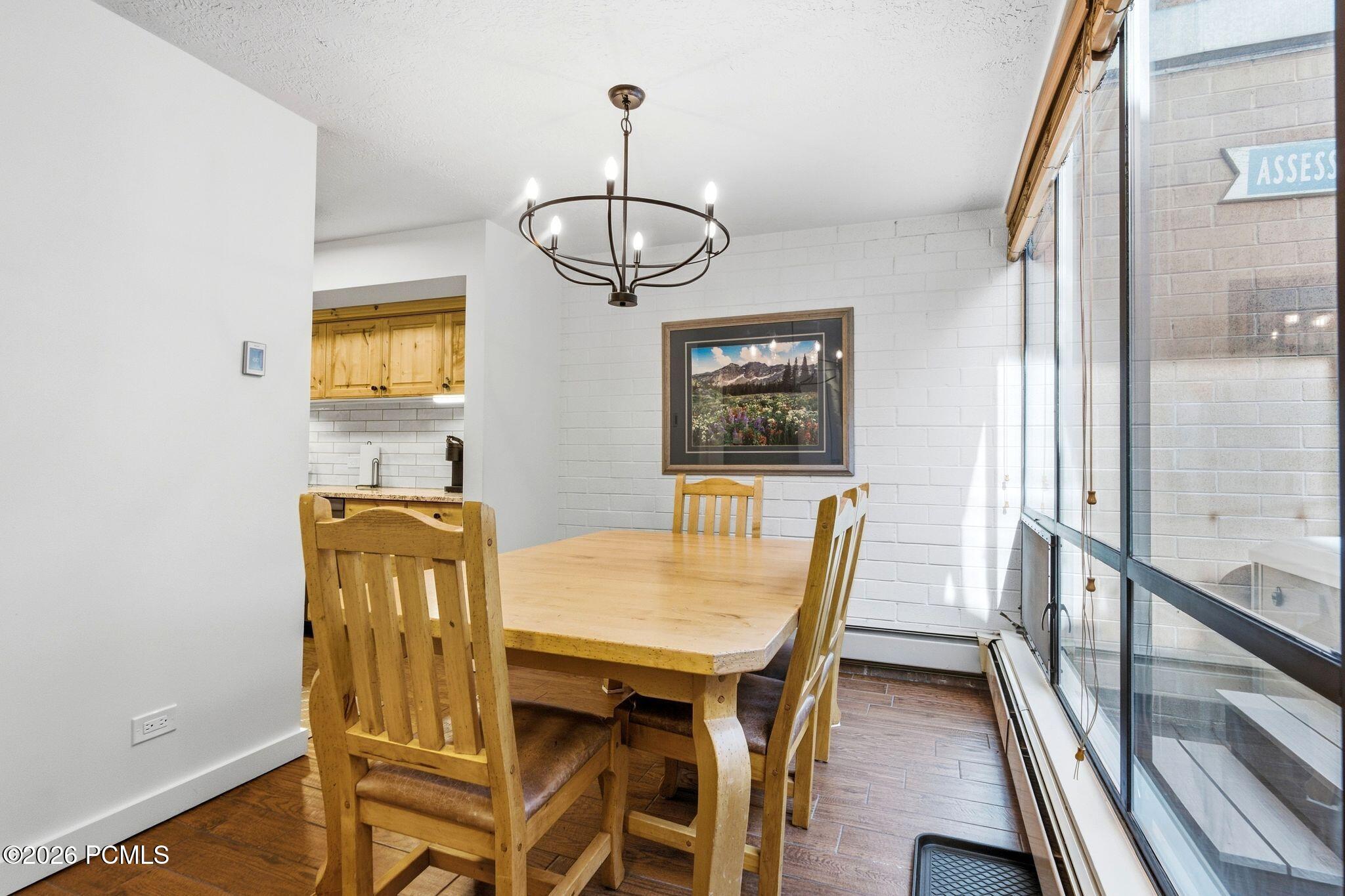 Dining area with a light wood table, chandelier, framed mountain landscape, and floor-to-ceiling windows.