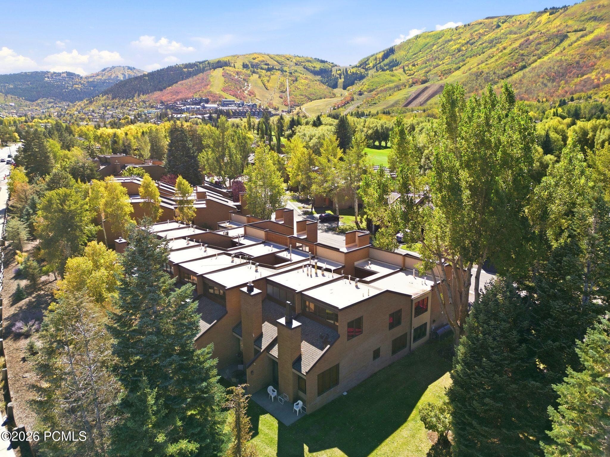 Aerial view of a townhouse community with flat roofs, colorful fall trees, and mountain slopes.