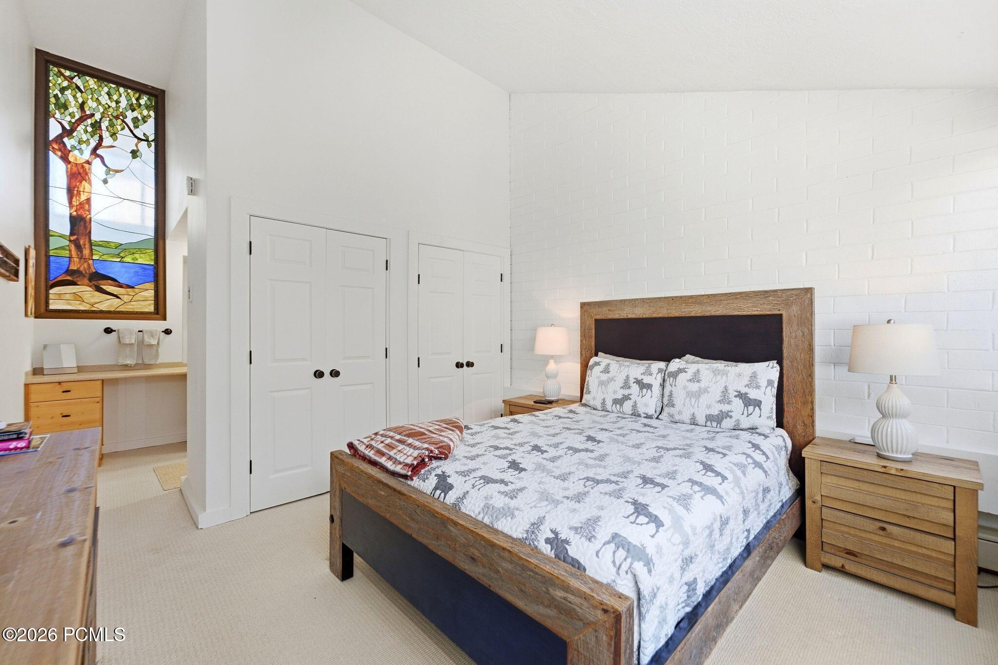 Bedroom with rustic wood bed, moose-pattern bedding, white brick wall, and stained-glass tree panel.