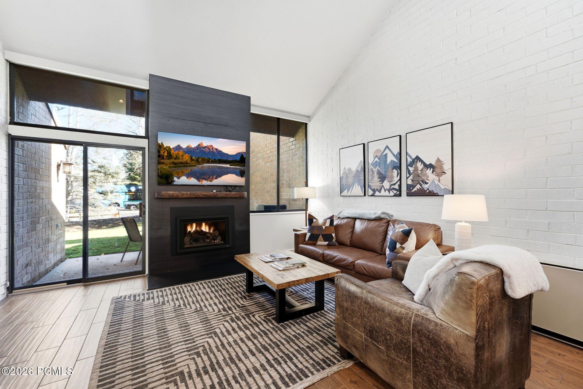 Living room with a central fireplace, leather seating, geometric rug, and sliding glass doors to a patio.