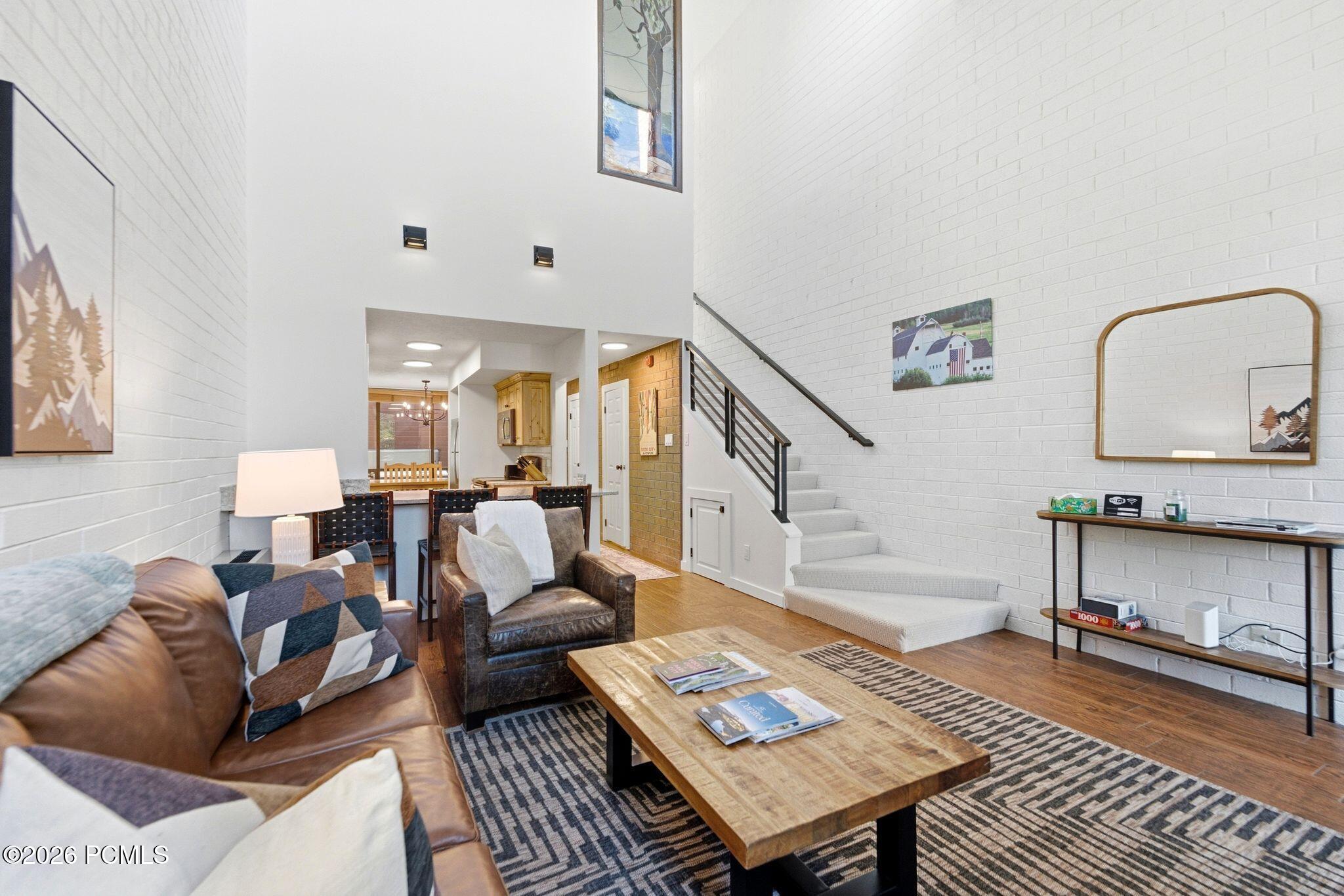 Double-height living room with leather sofas, white brick walls, and a staircase with dark metal railings.