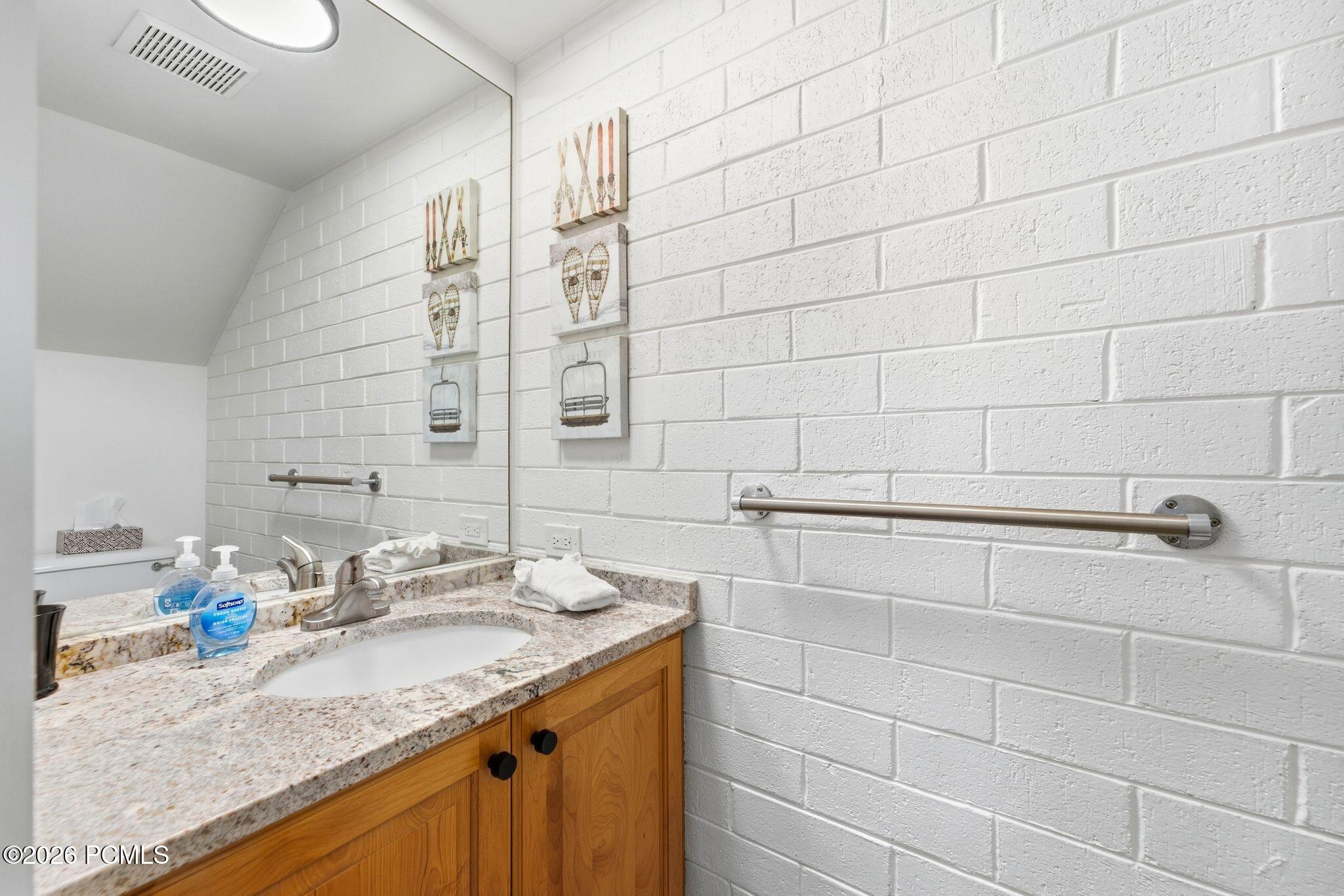 Bathroom vanity with a speckled stone countertop, wood cabinets, and a stainless-steel wall grab bar.