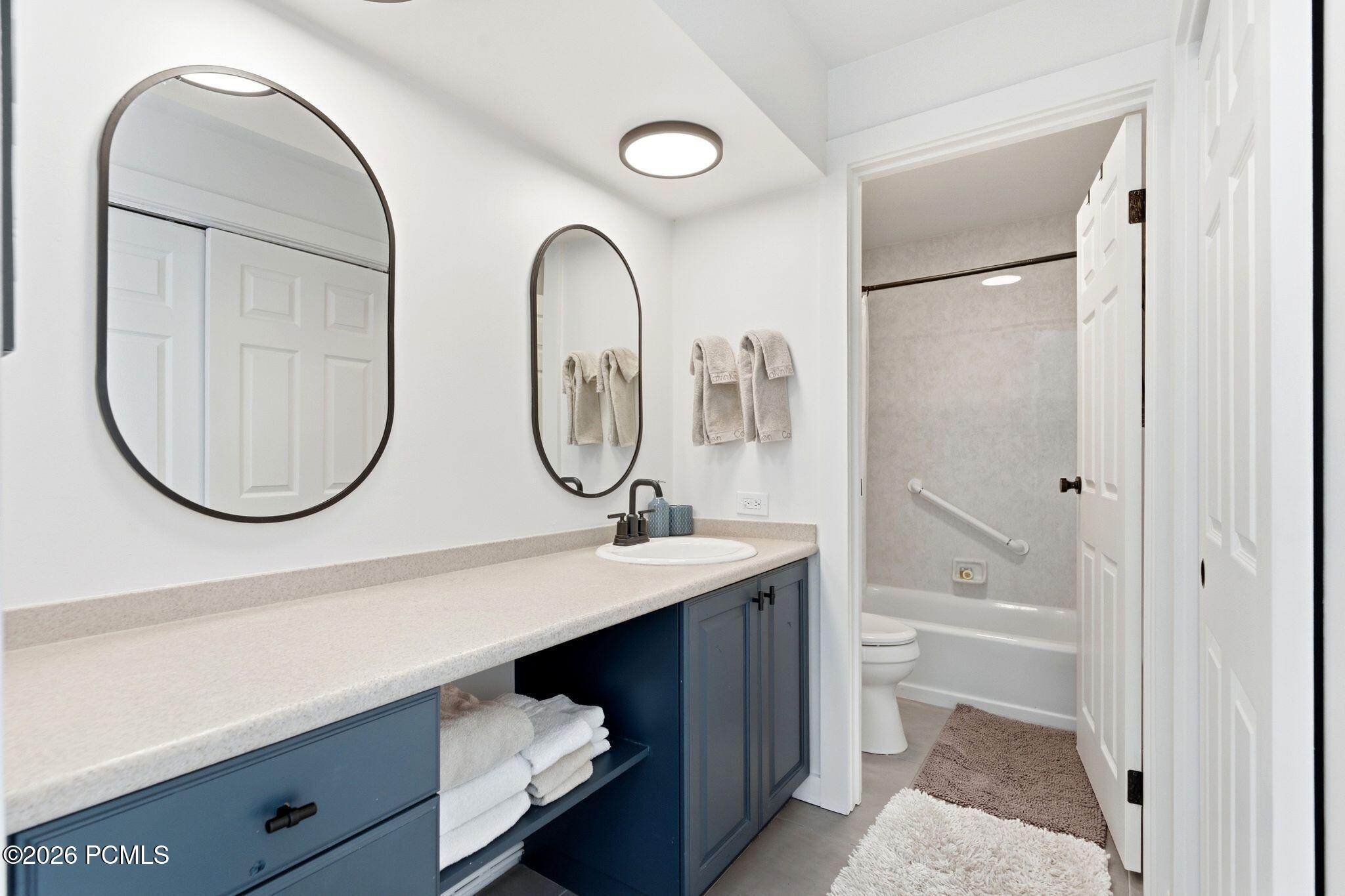 Bathroom with blue vanity cabinets, arched mirrors, and a tub-shower with a grab bar.