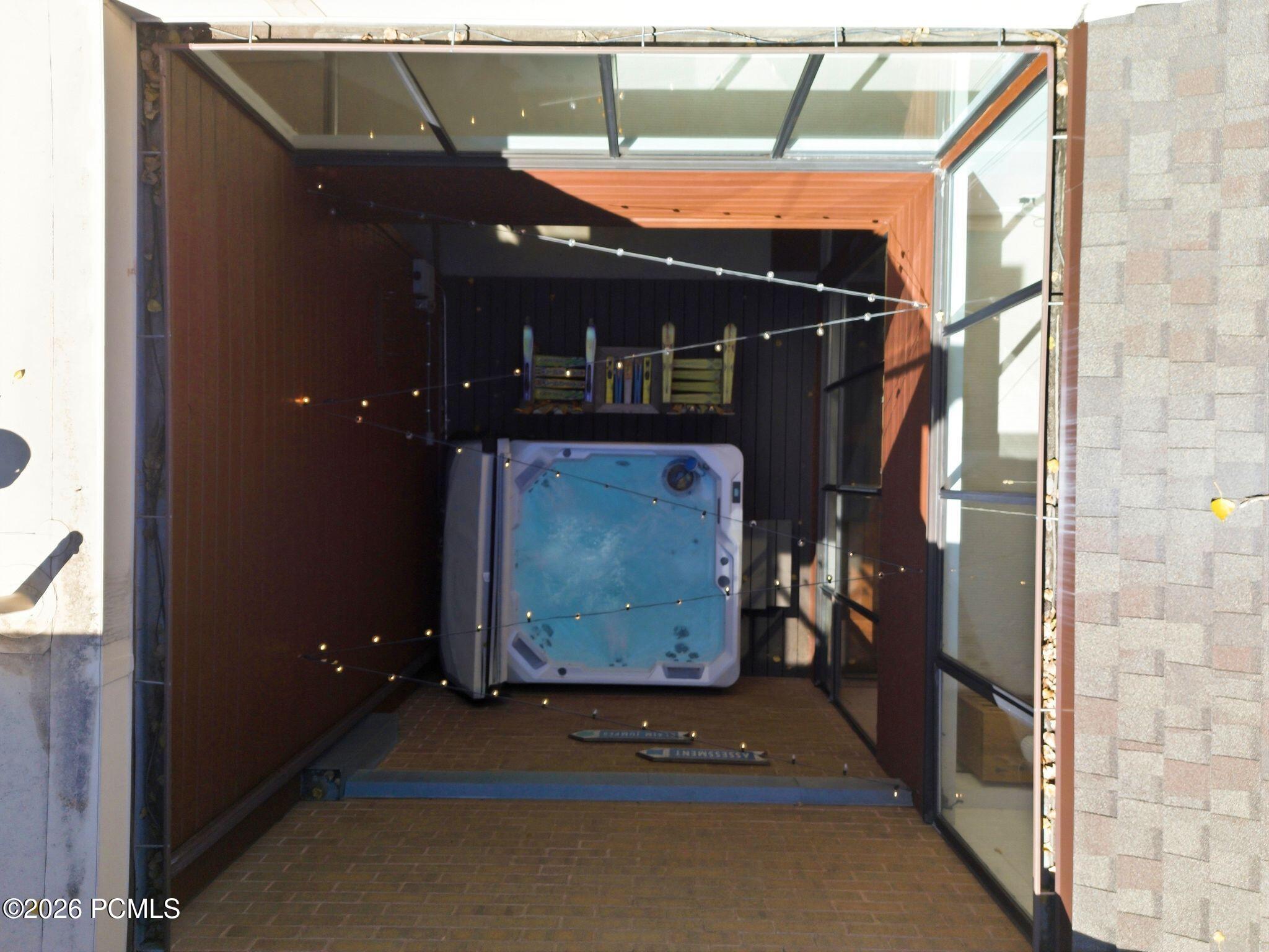 Covered patio with a built-in hot tub, glass roof, brick floor, and string lights.