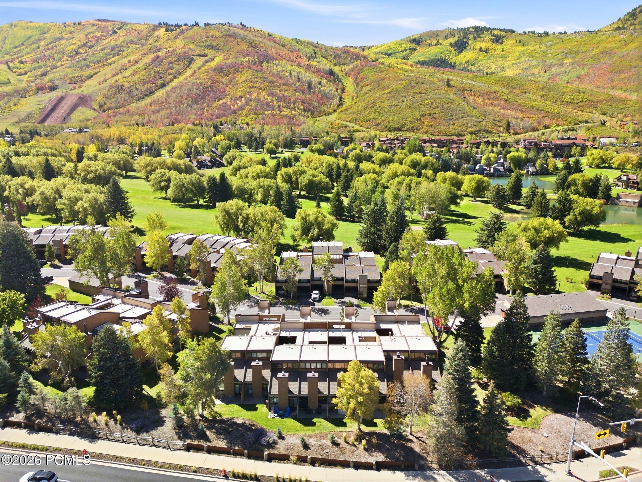 Aerial view of condominium homes and green lawns beneath autumn-colored Park City hills.