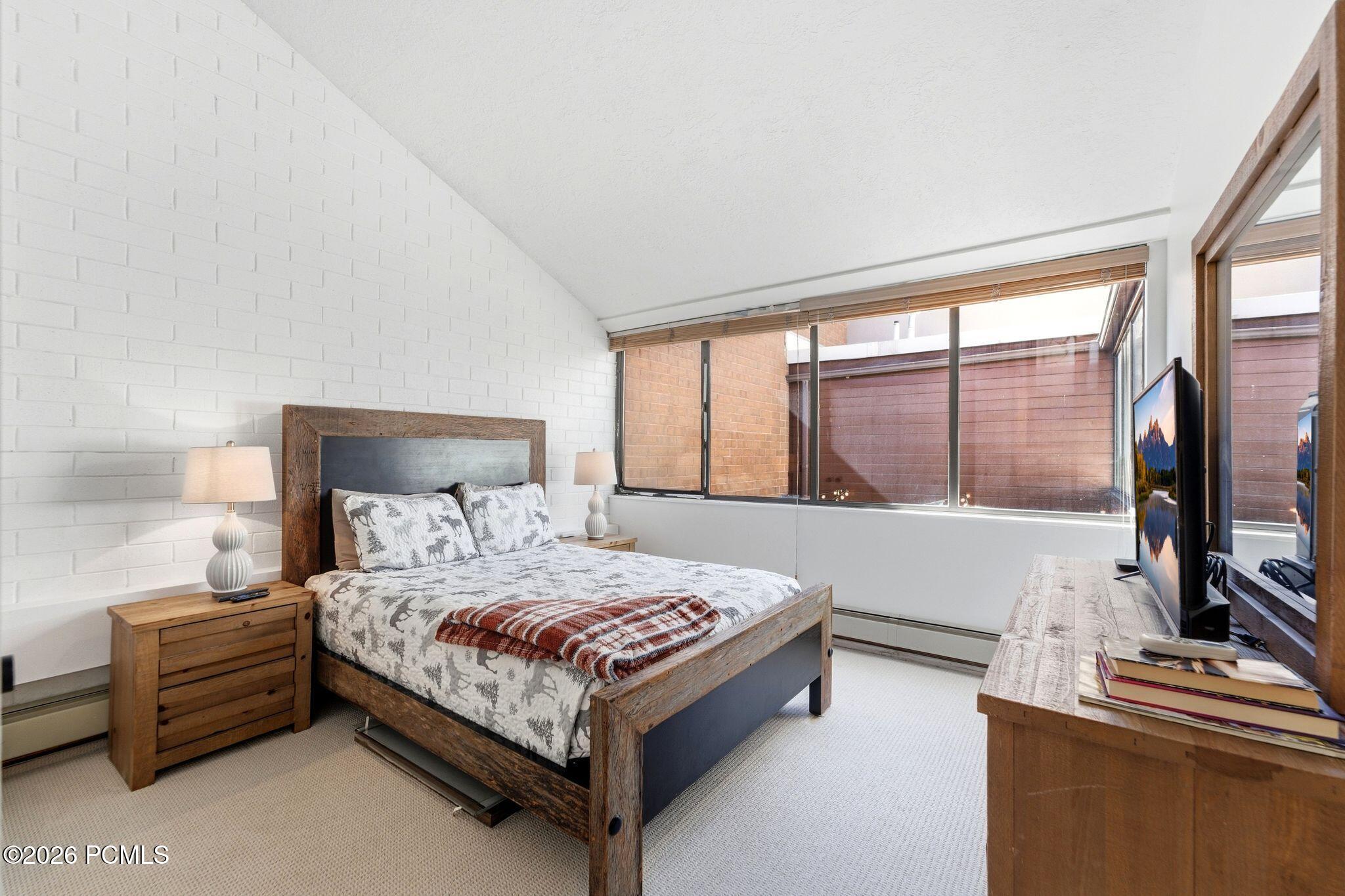 Bedroom with a rustic wood bed, patterned bedding, and large windows.