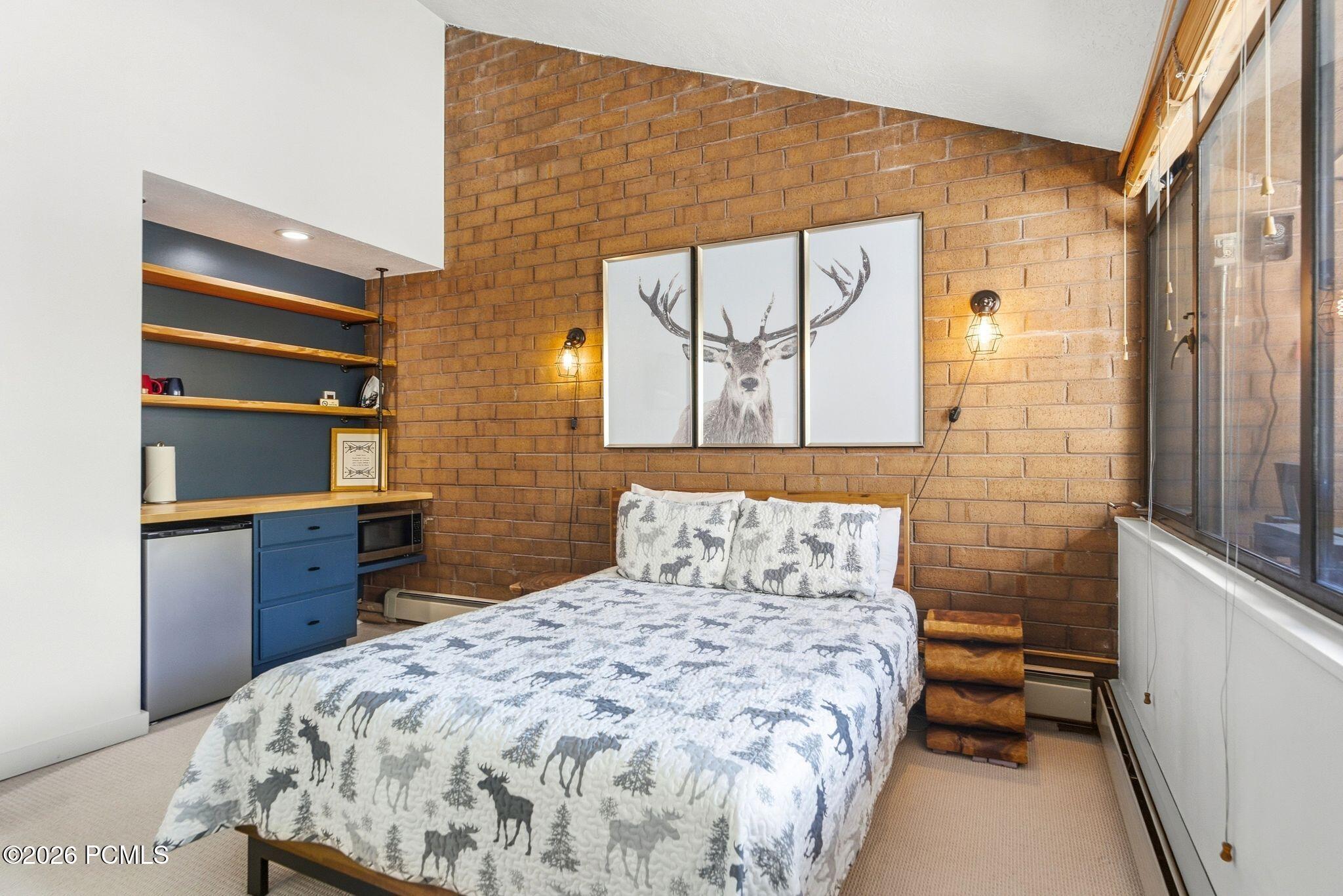 Bedroom with a wildlife-patterned bed, brick accent wall, and large windows.