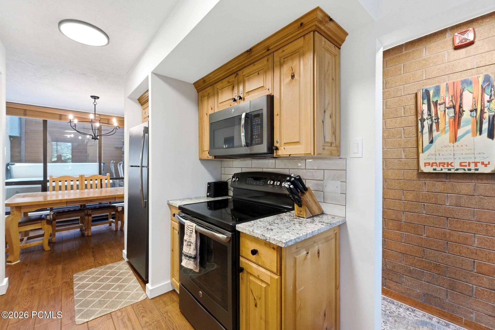 Kitchen with wood cabinets, granite counters, black range, and dining table beside large windows.