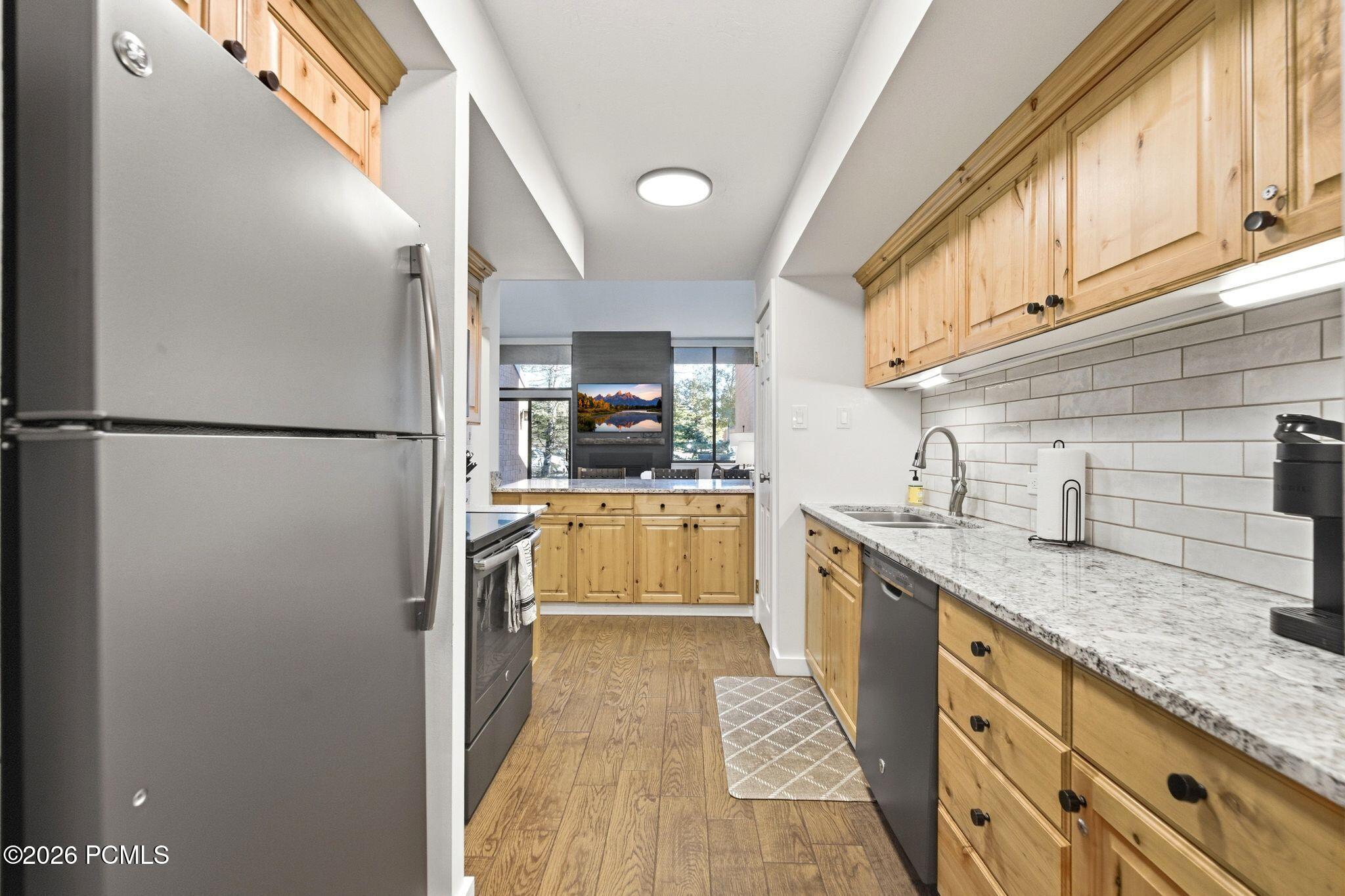 Galley kitchen with light wood cabinets, granite counters, and a stainless steel refrigerator.
