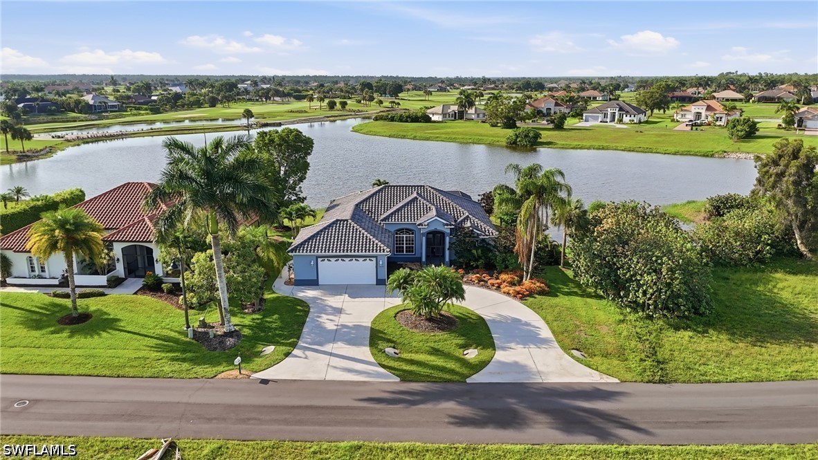 Blue tile-roofed home with a curved driveway, landscaped lawn, and lake behind it.