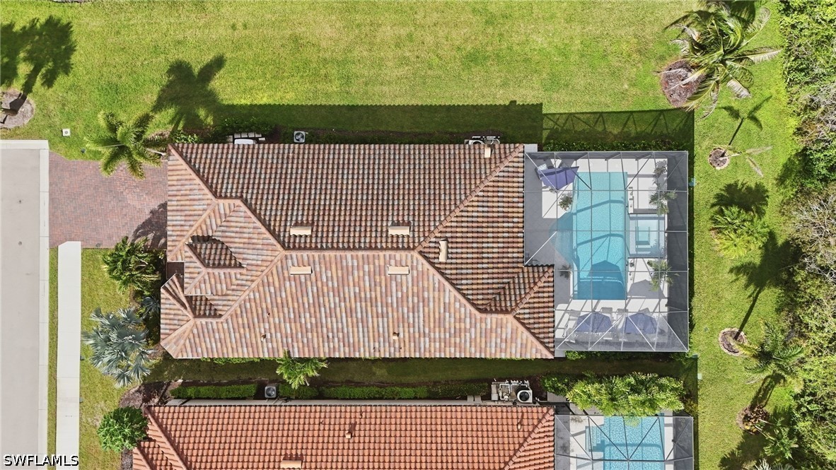 Aerial view of a tile-roofed home with a screened pool and palm-dotted lawn.