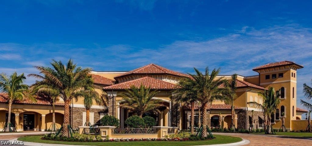 Mediterranean-style clubhouse with terracotta roofs, stone accents, and a palm-lined entrance.