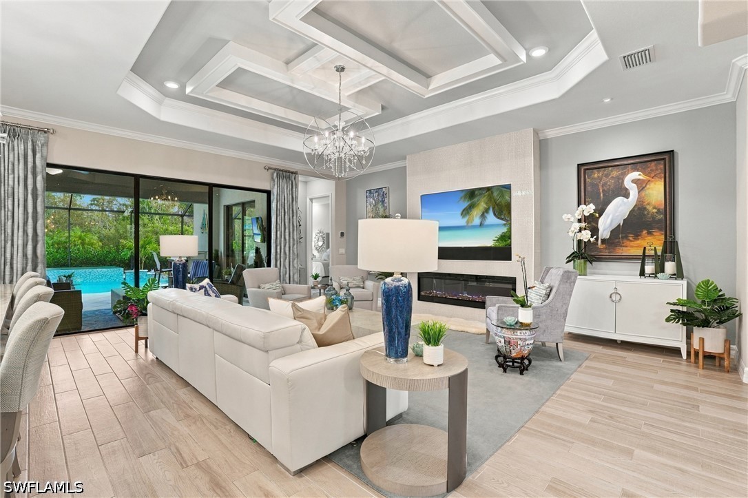Living room with a tray ceiling, chandelier, fireplace, and sliding doors overlooking the pool.