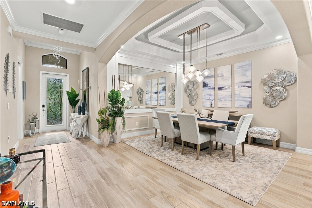 Dining room with a long table beneath pendant lights, beside a decorative glass entry door.