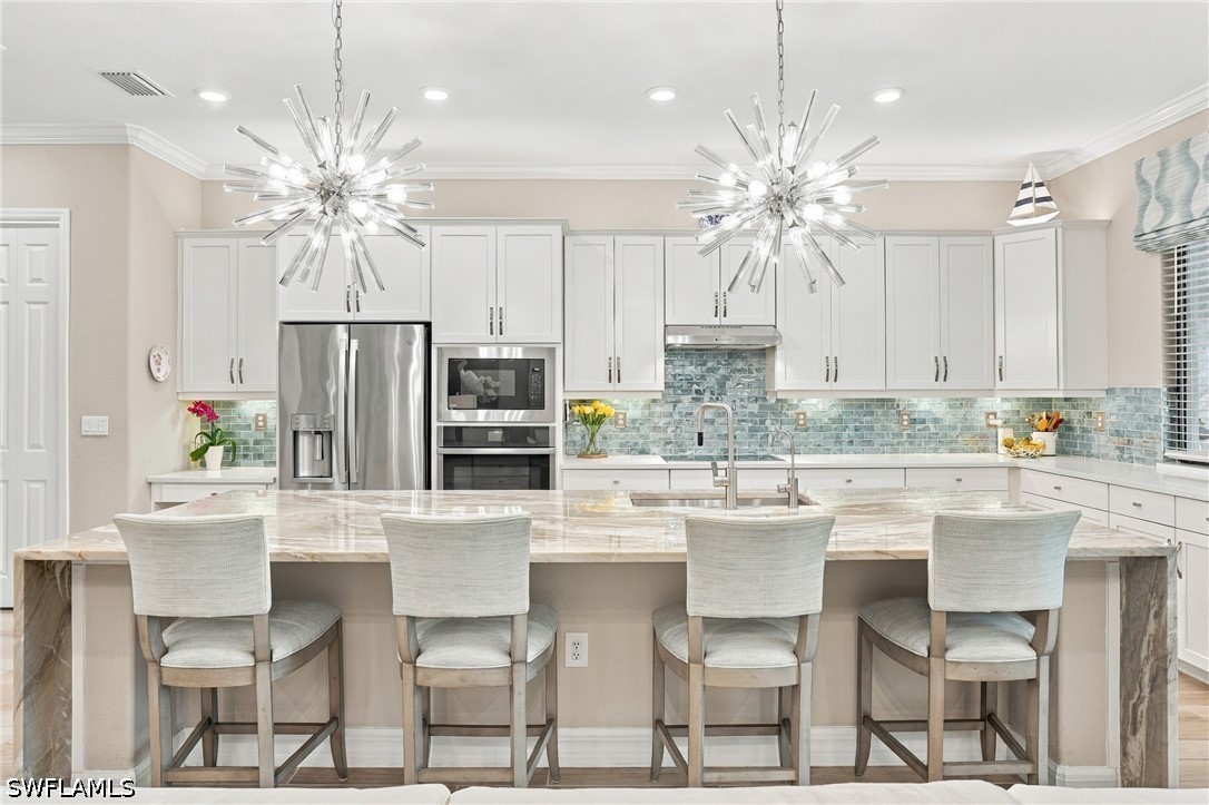 Kitchen with a marble island, four stools, white cabinets, and a blue-green tile backsplash.