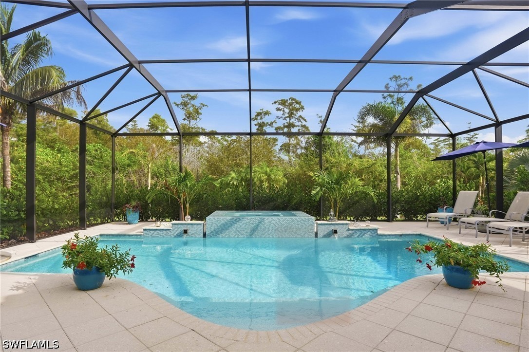 Swimming pool and raised tiled spa beneath a screened enclosure, with tropical landscaping and lounge chairs.