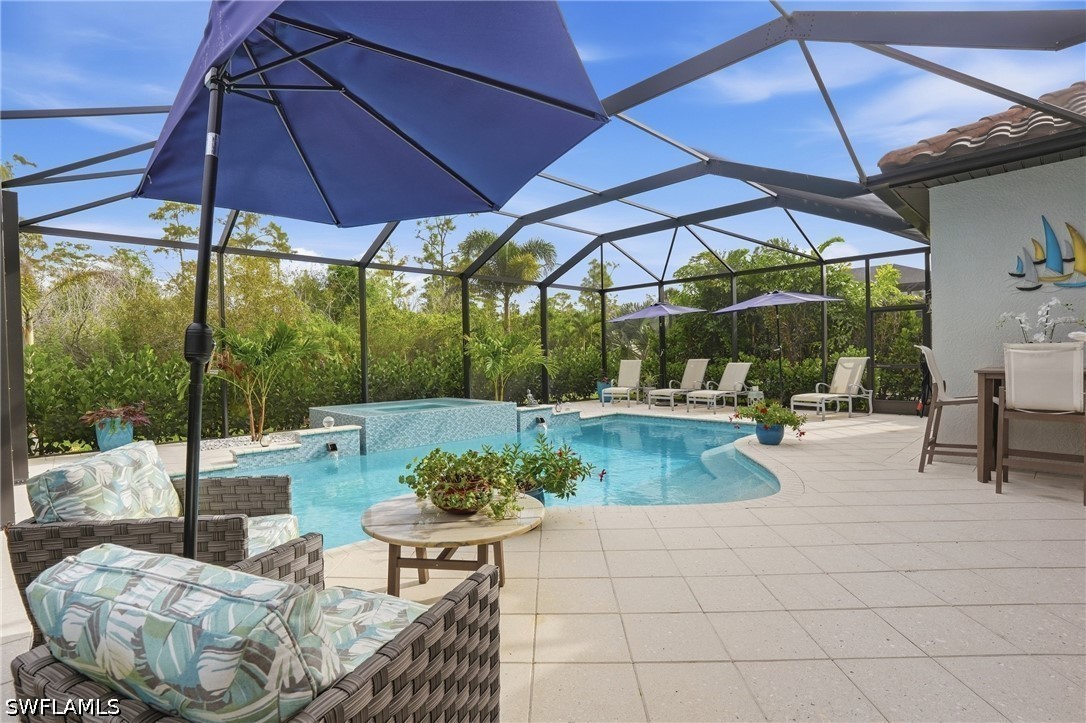 Screened pool patio with a raised spa, lounge chairs, and tropical greenery.