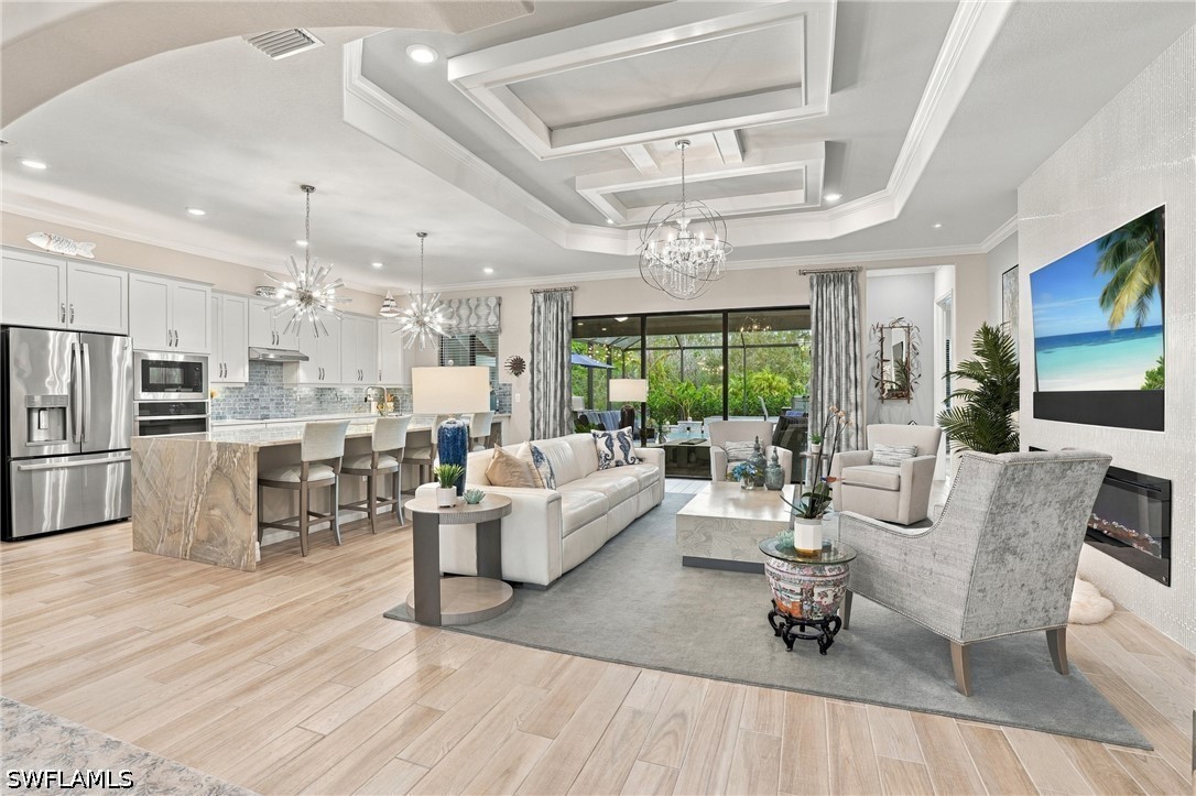 Open-plan living room and kitchen with a marble island, tray ceiling, and sliding doors to greenery.