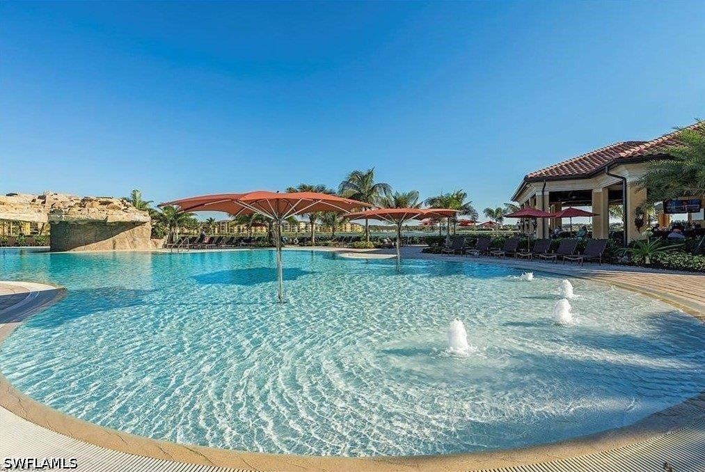 Community pool with a shallow entry, fountains, shade umbrellas, and a covered pavilion.