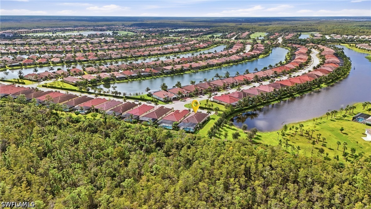 Aerial view of homes lining winding canals beside a wooded preserve, with a yellow marker over one home.