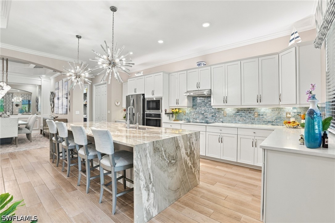 Bright kitchen with white cabinets, blue-gray tile backsplash, and a large marble waterfall island.