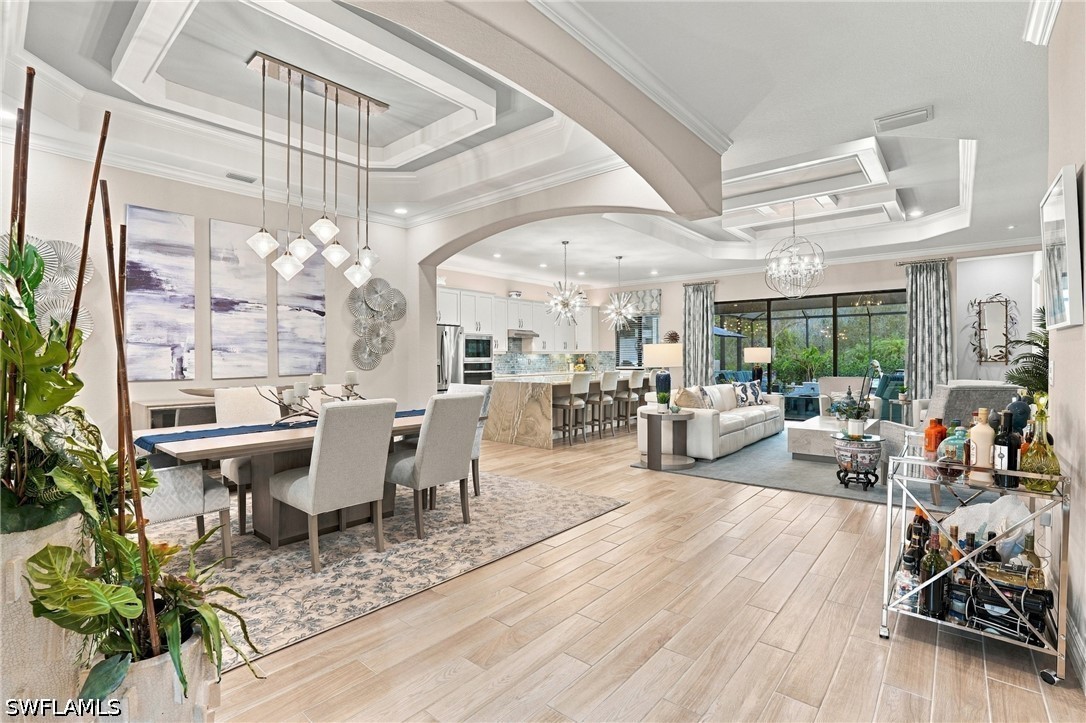 Open-plan dining and living area with a large kitchen, tray ceilings, and sliding glass doors.