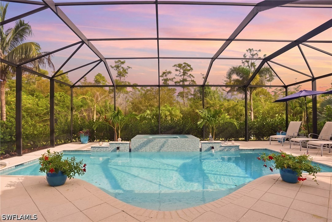 Screened backyard pool and raised spa surrounded by tropical landscaping at dusk.