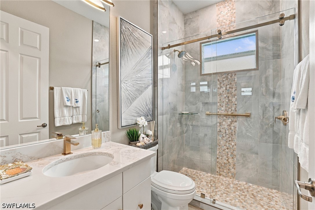 Bathroom with a marble-look vanity and glass shower featuring pebble mosaic accents.