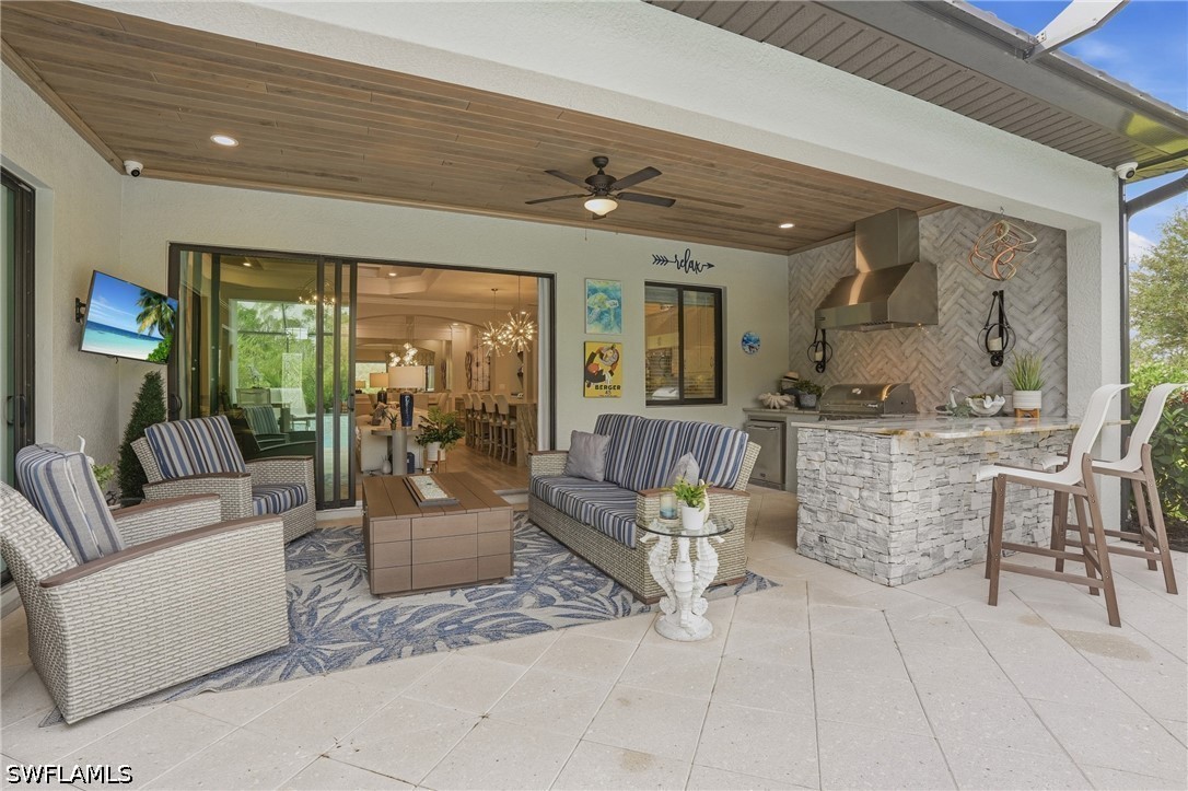 Covered patio with wicker seating and a stone outdoor kitchen beside sliding glass doors.
