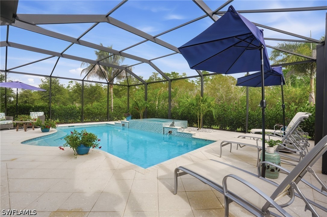 Backyard pool under a screened lanai, with lounge chairs, blue umbrellas, and a raised tiled water feature.
